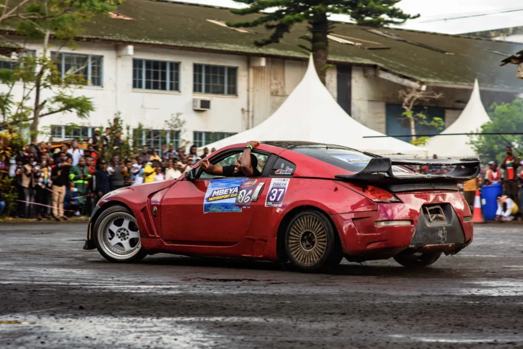 A red Nissan 350Z drifting on wet tarmac in front of the crowd at Arusha Drift Car Park